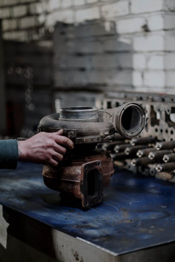 A close-up of a mechanic's hand holding a turbocharger on a workbench in a workshop.